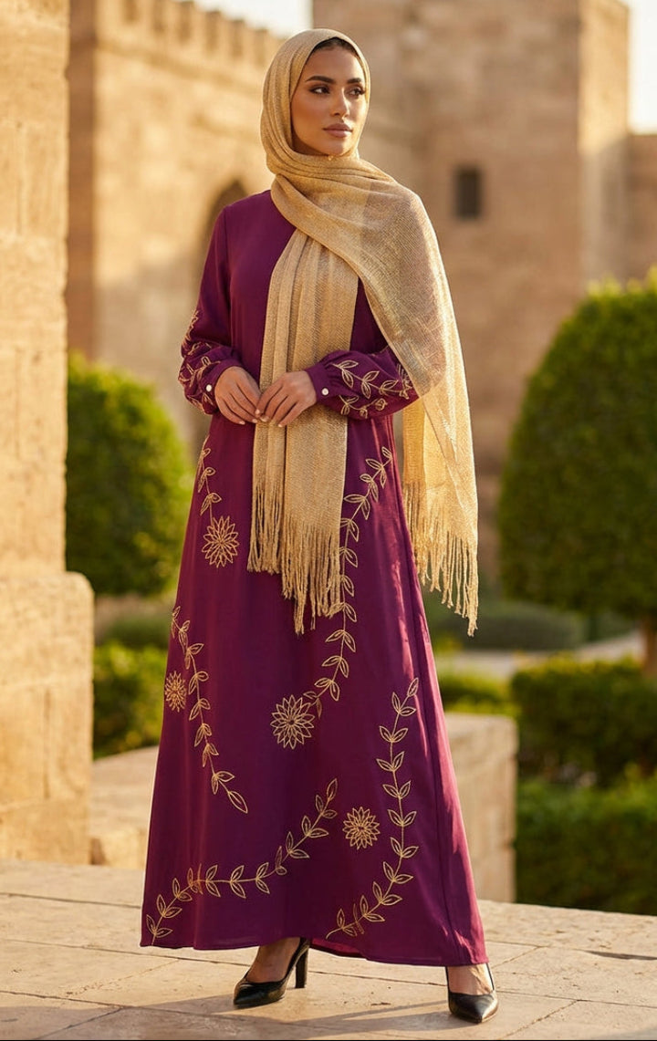 Woman in a purple dress with gold embroidery and beige hijab standing in front of a stone building.