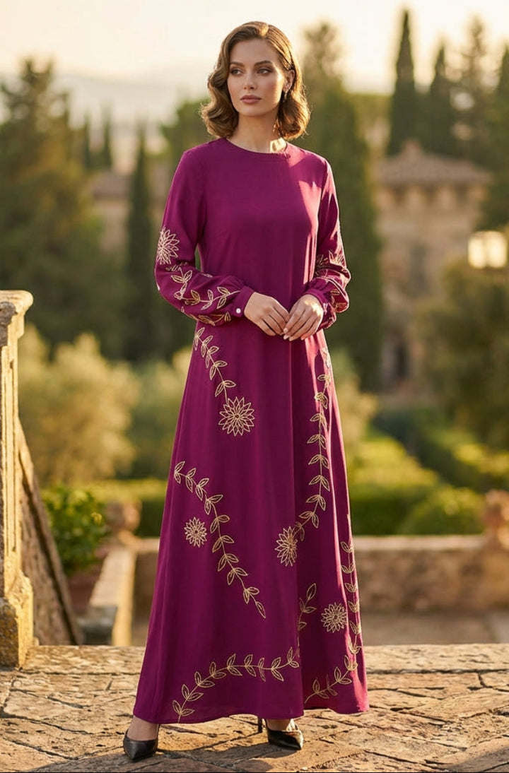 Woman in a purple dress with floral patterns standing in an outdoor setting with greenery and a building in the background.