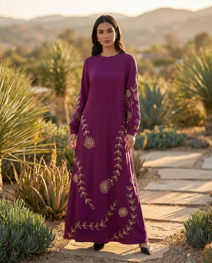Woman in a purple dress with gold embroidery standing in a desert landscape.