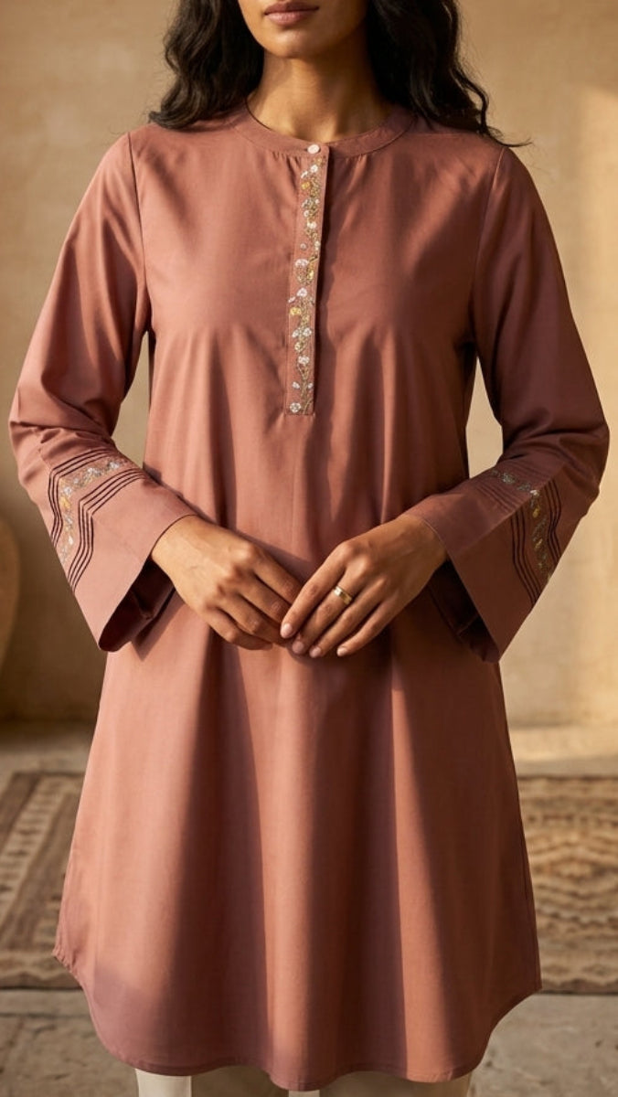 Woman wearing a pink kurta in a warm-toned room with a vase and rug.