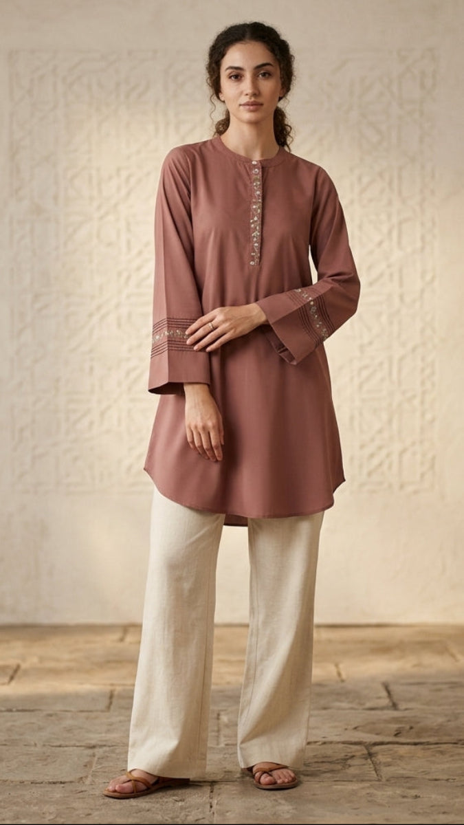 Woman wearing a brown embroidered top and white pants in a studio setting