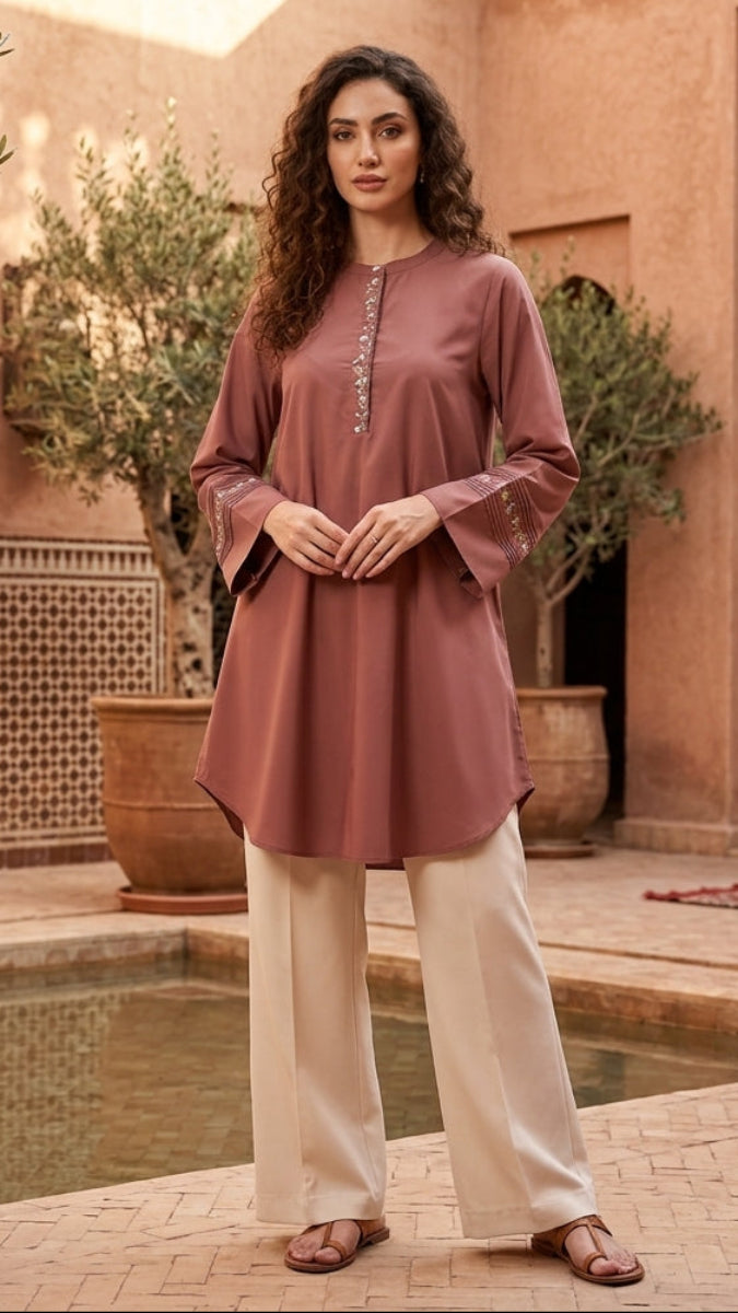 Woman in a pink top and white pants standing in a courtyard with a pool and traditional architecture.