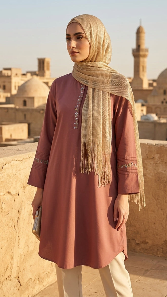 Woman in a pink dress and beige hijab standing on a rooftop with architectural landmarks in the background.