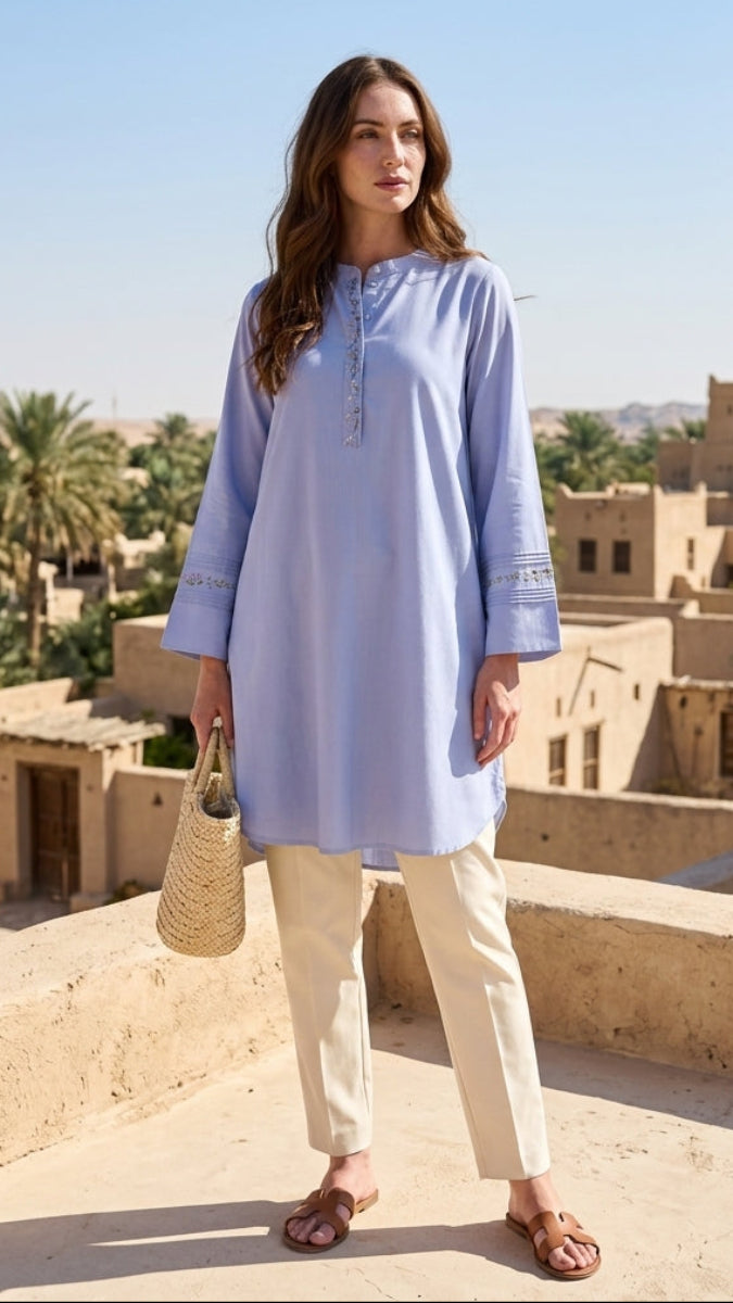 Woman in a light blue dress standing on a rooftop with desert architecture in the background