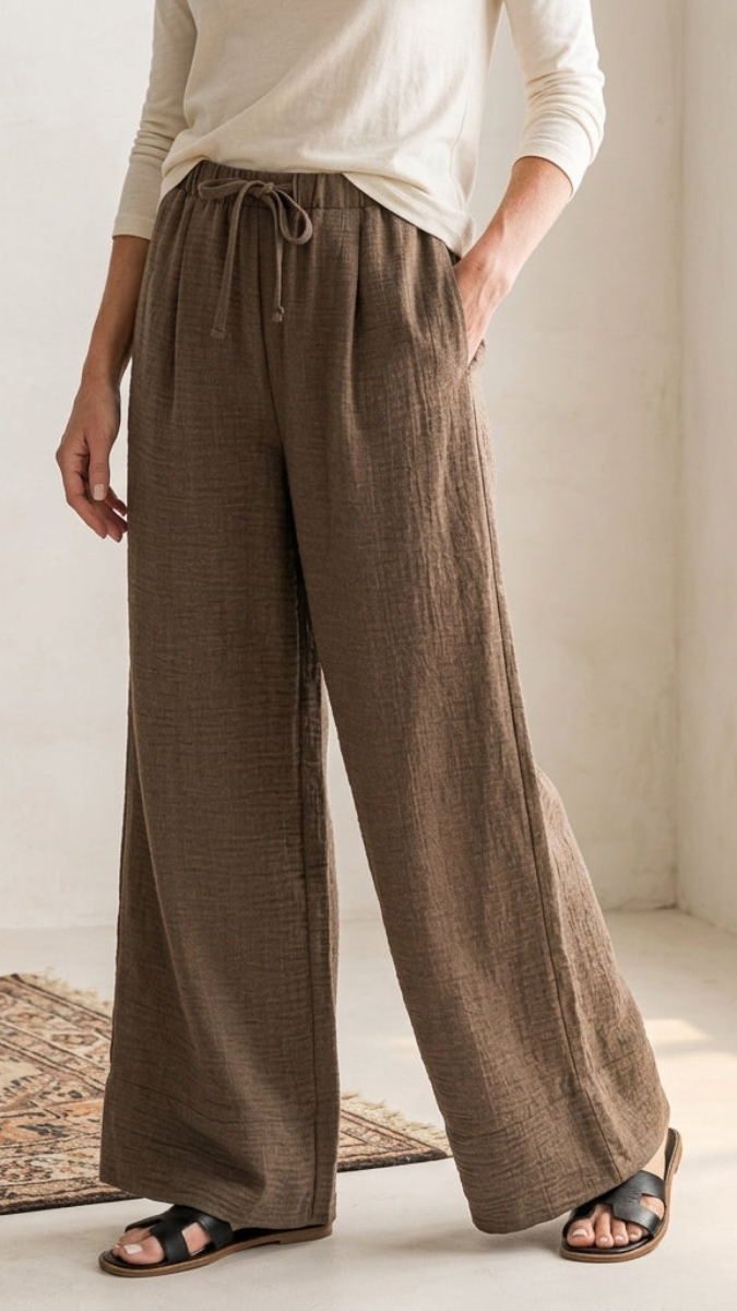 Person wearing brown wide-leg pants in a bright room with a lamp and rug.