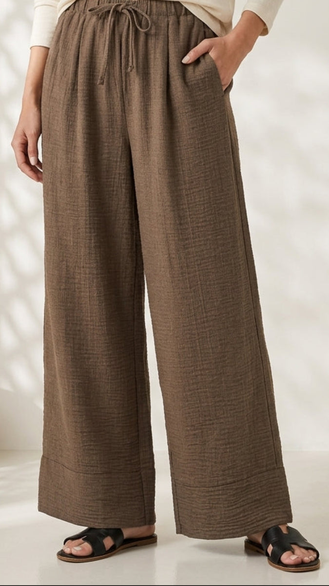 Person wearing brown wide-leg pants with a white top in a minimalistic setting.
