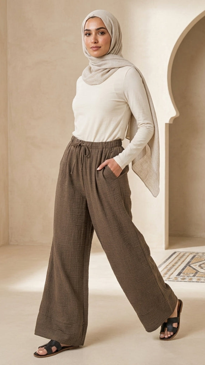Woman wearing a hijab and white top with brown pants in a neutral setting