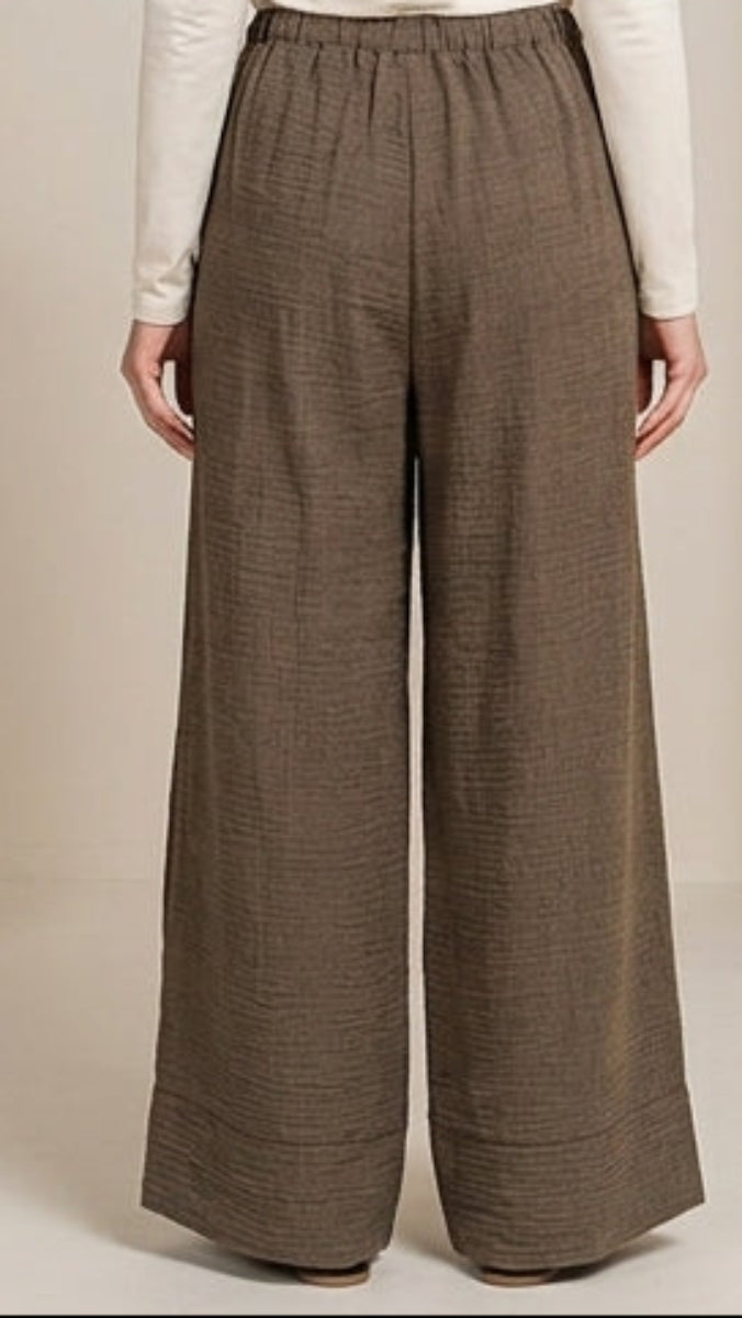 Person wearing a beige hijab and brown wide-leg pants standing in a neutral setting.