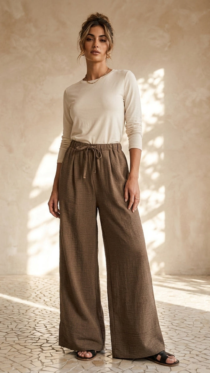 Woman wearing a beige top and brown wide-leg pants in a sunlit room.