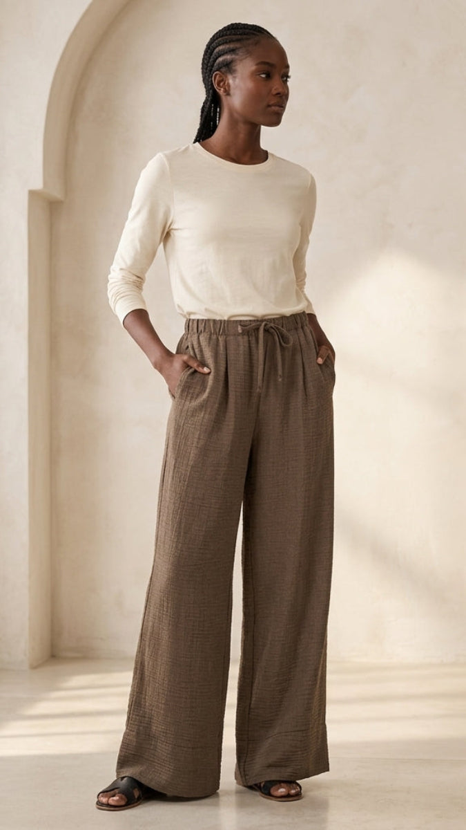 Woman wearing a white top and brown wide-leg pants in a softly lit room.