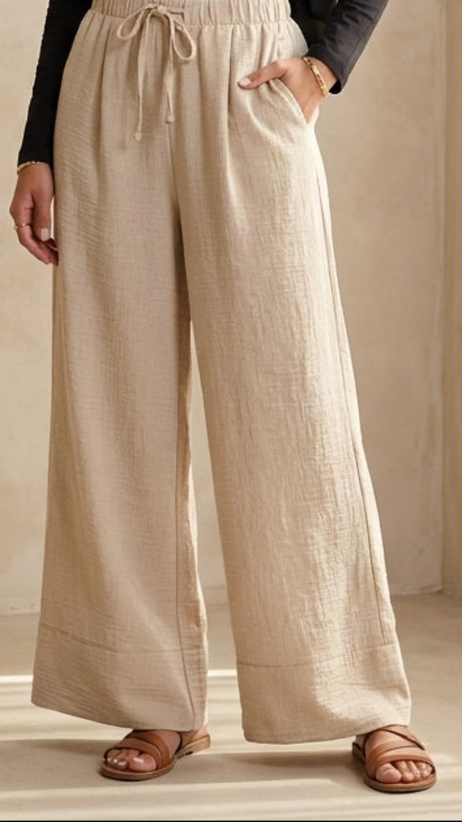 Woman wearing a black top and beige pants standing in a softly lit room.