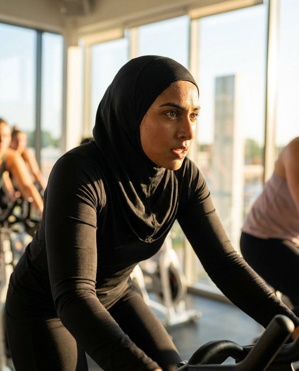 Woman wearing a hijab exercising on a stationary bike in a gym.