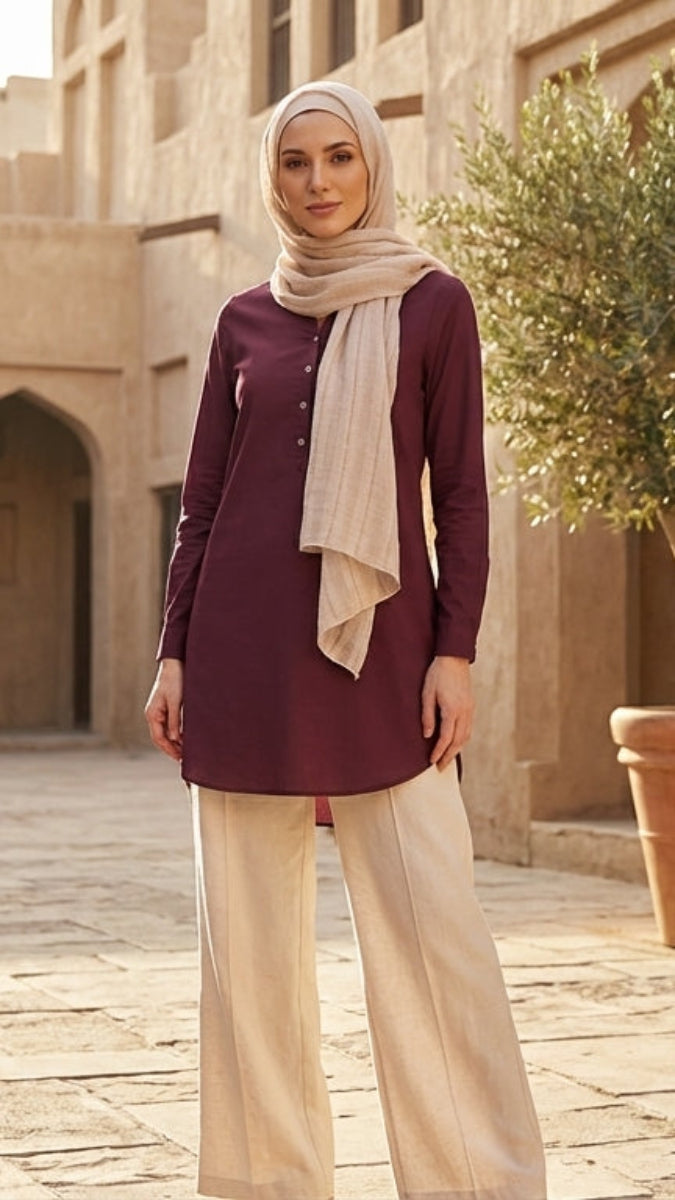 Woman in traditional attire standing in a courtyard with architectural elements and a potted plant.