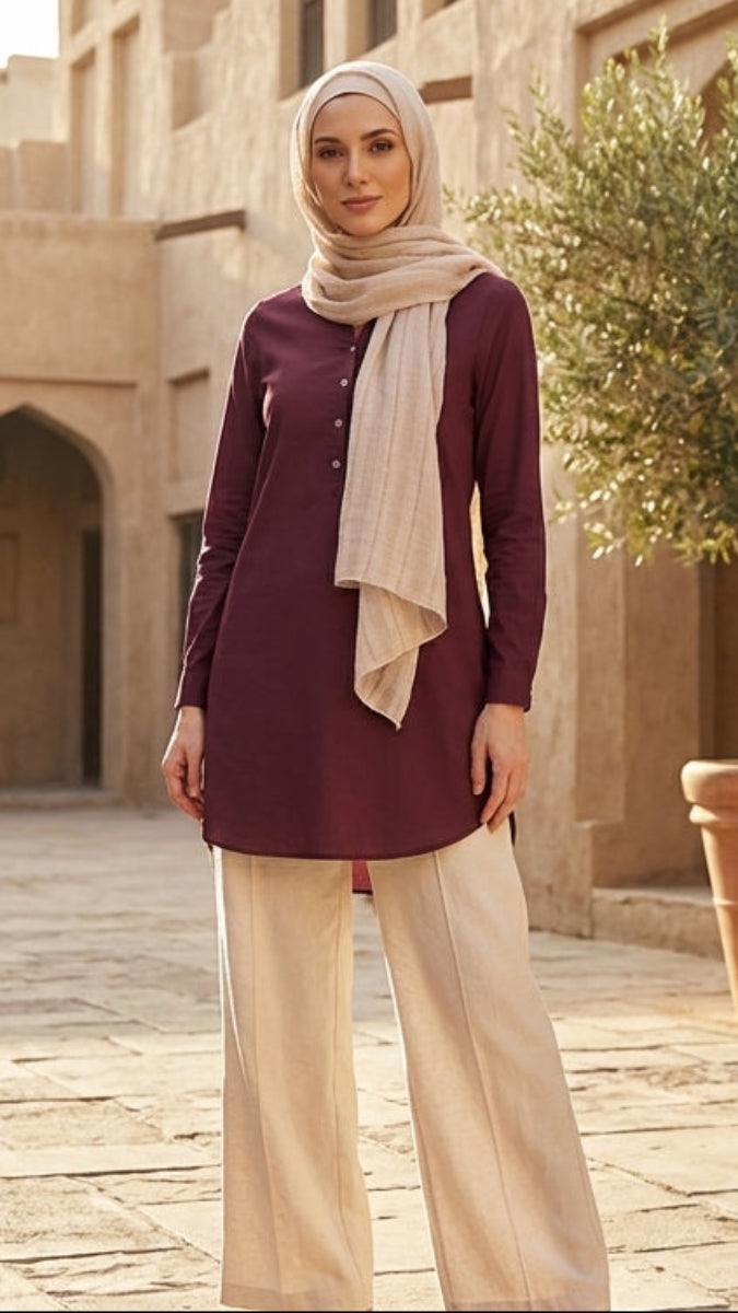 Woman in maroon tunic standing in a courtyard with architectural elements and a potted plant.