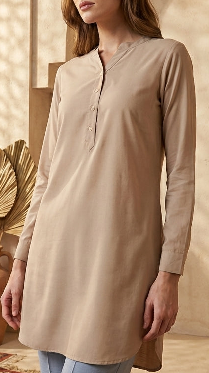 Woman in a beige long-sleeve shirt standing in a warm-toned interior setting with decorative plants and vases.
