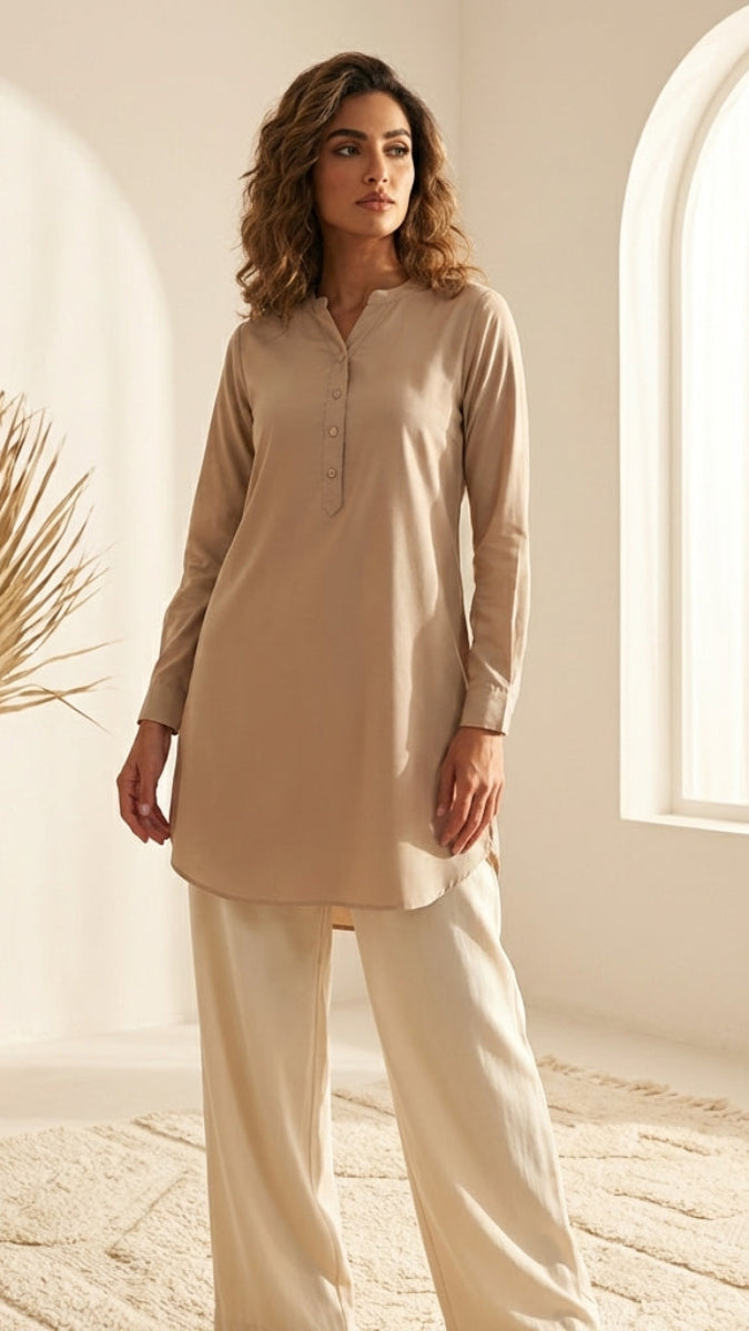 Woman wearing a beige outfit standing in a bright room with a vase of dried plants.