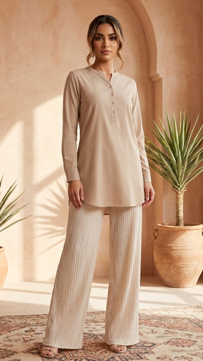 Woman in beige outfit standing in a sunlit room with plants