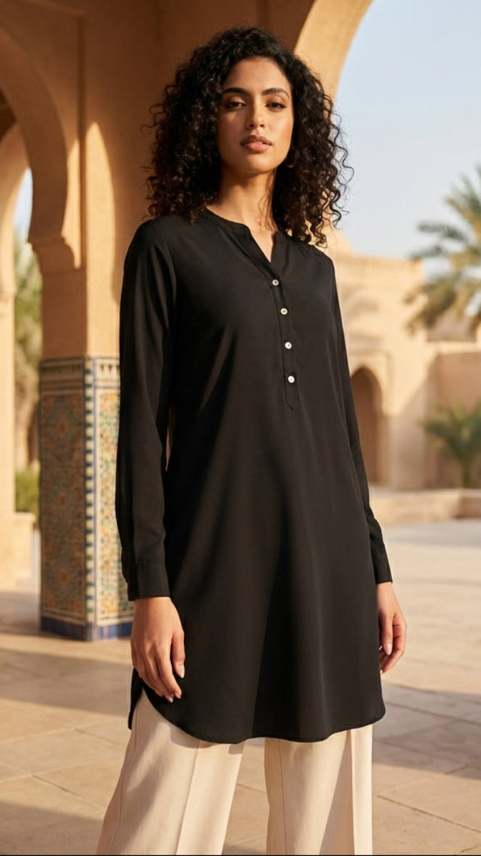 Woman wearing a black long-sleeve top and white pants standing in a sunlit courtyard with arches and palm trees.