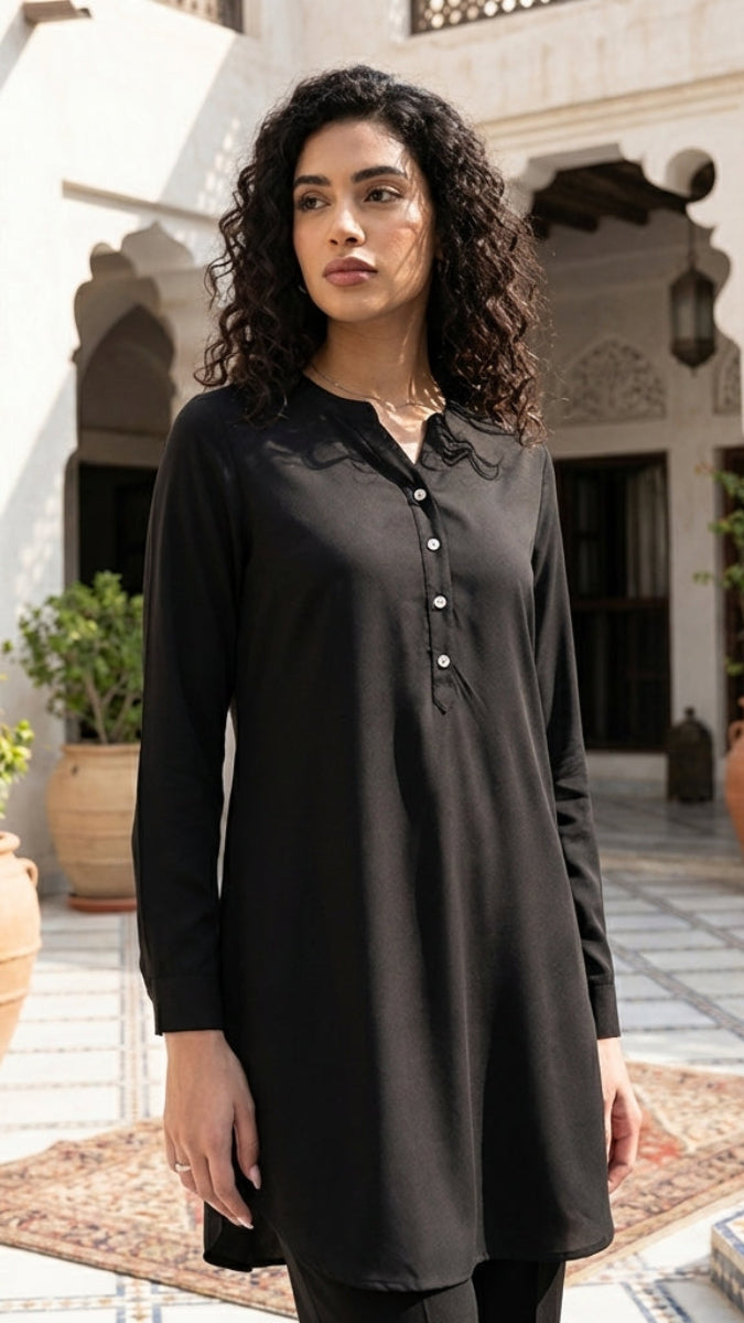 Woman wearing a black tunic in an outdoor setting with architectural elements and plants.