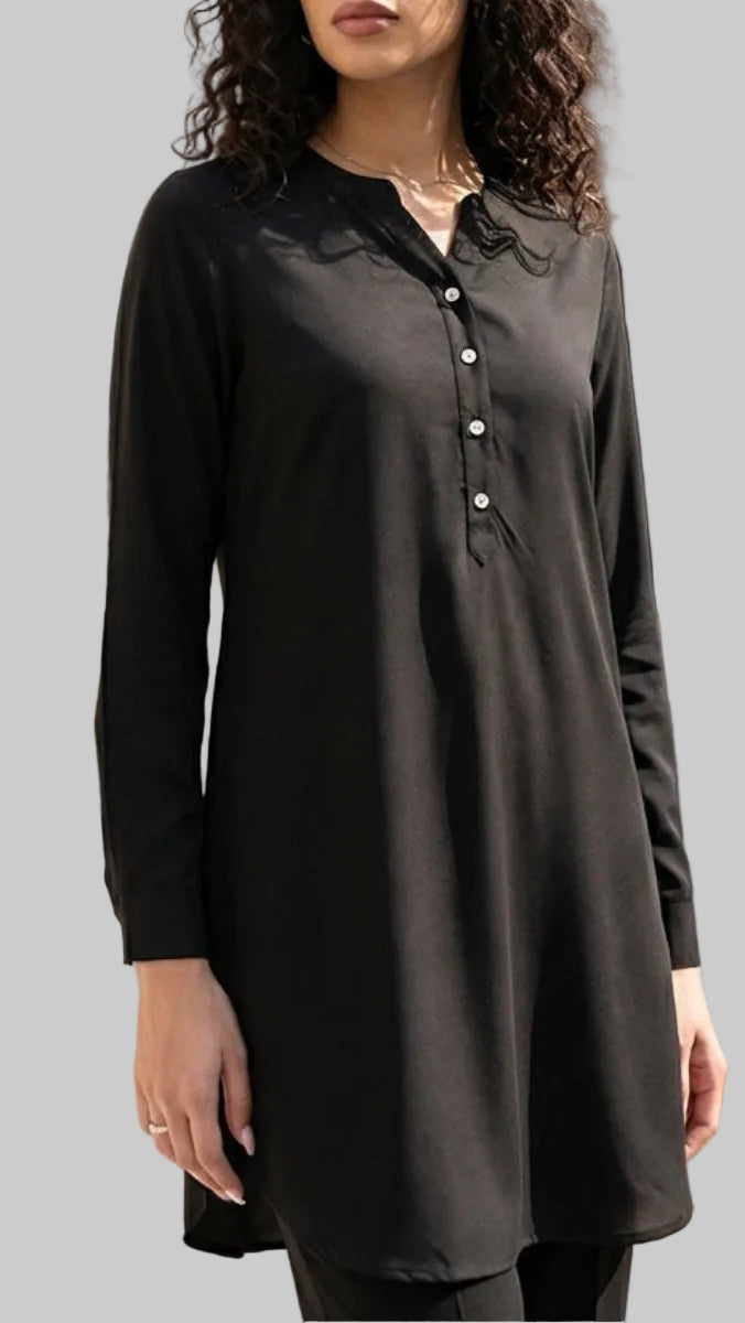 Woman wearing a black tunic in an outdoor setting with architectural elements and plants.