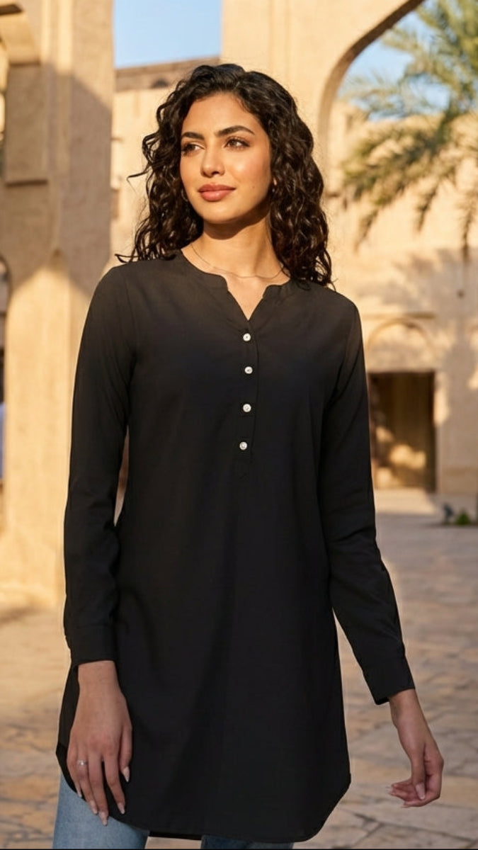 Woman in a black long-sleeve top standing in front of traditional architecture with arches and palm trees.