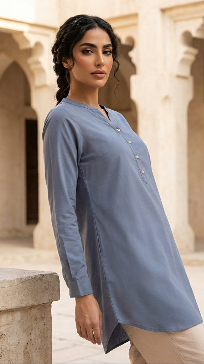 Woman wearing a blue long-sleeve top in an outdoor setting with stone architecture.