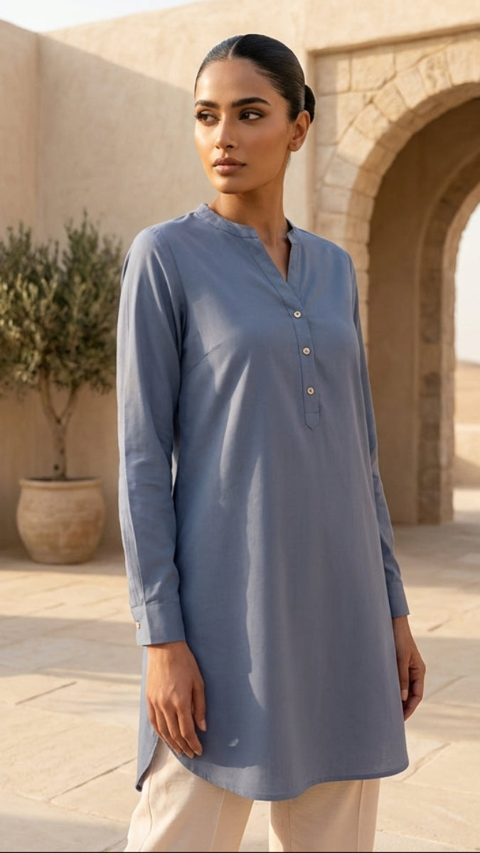 Woman wearing a blue long-sleeve shirt in a desert setting with arches and potted plants.