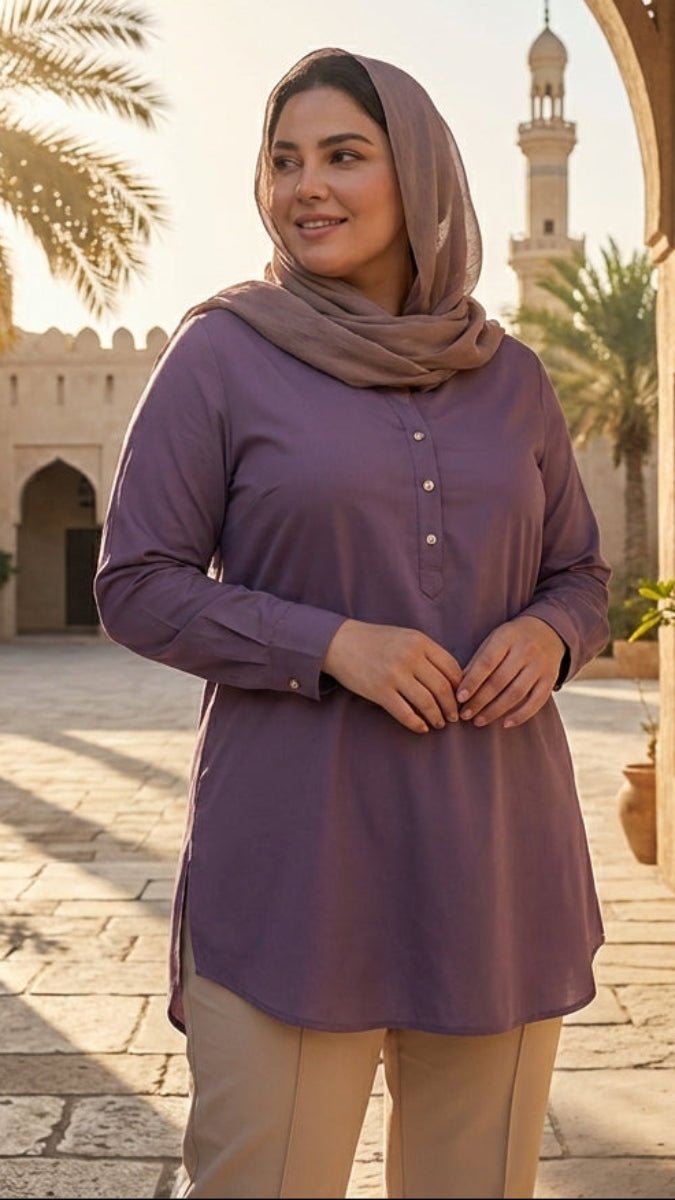 Woman in a purple shirt and hijab standing in a sunlit courtyard with arches and palm trees.
