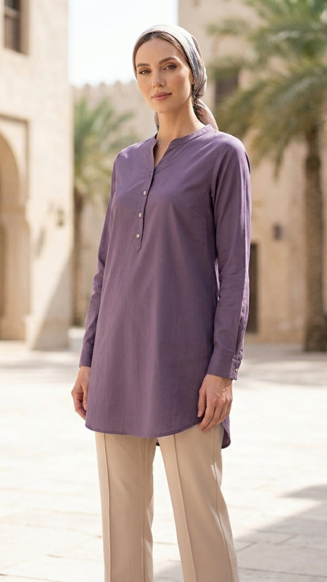 Woman wearing a long-sleeve purple shirt and beige pants standing in front of a building with palm trees.