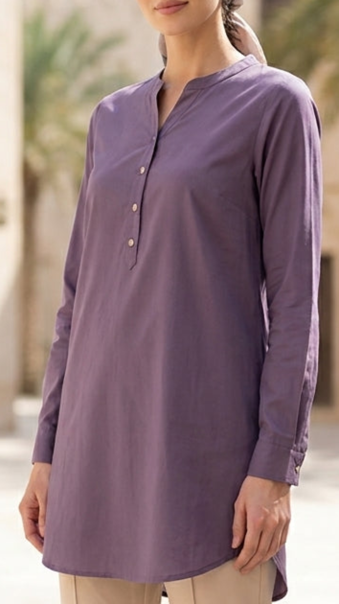 Woman wearing a long-sleeve purple shirt and beige pants standing in front of a building with palm trees.