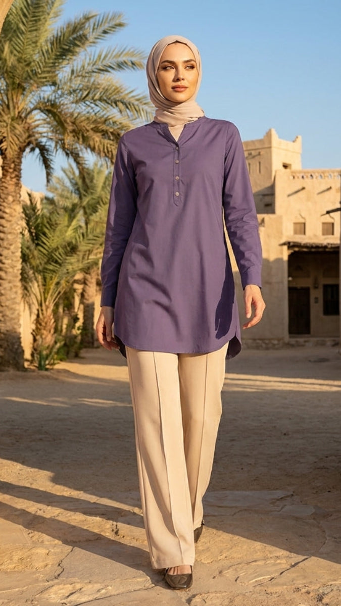 Woman in a purple top and beige hijab walking through an archway with palm trees and buildings in the background.