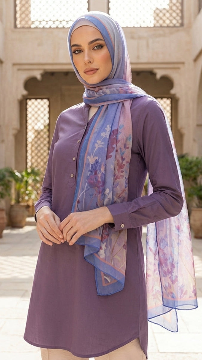 Woman wearing a purple outfit with a floral scarf in an outdoor setting with arches and plants.