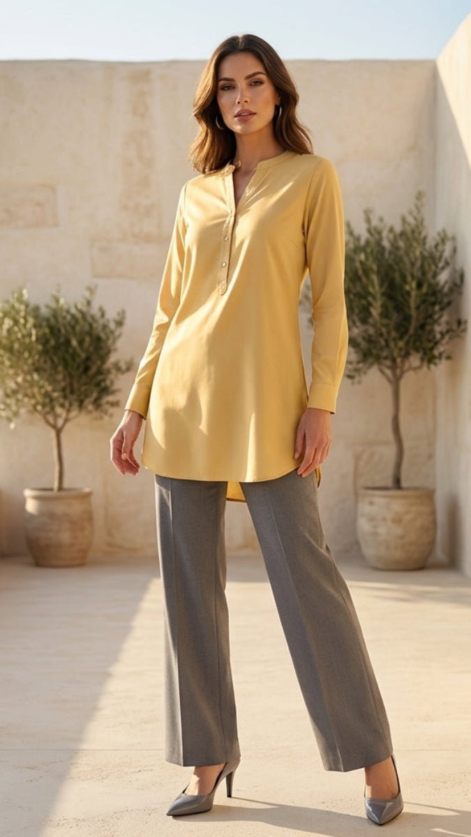 Woman in a yellow top and gray pants standing on a sunlit patio with plants and a scenic background.
