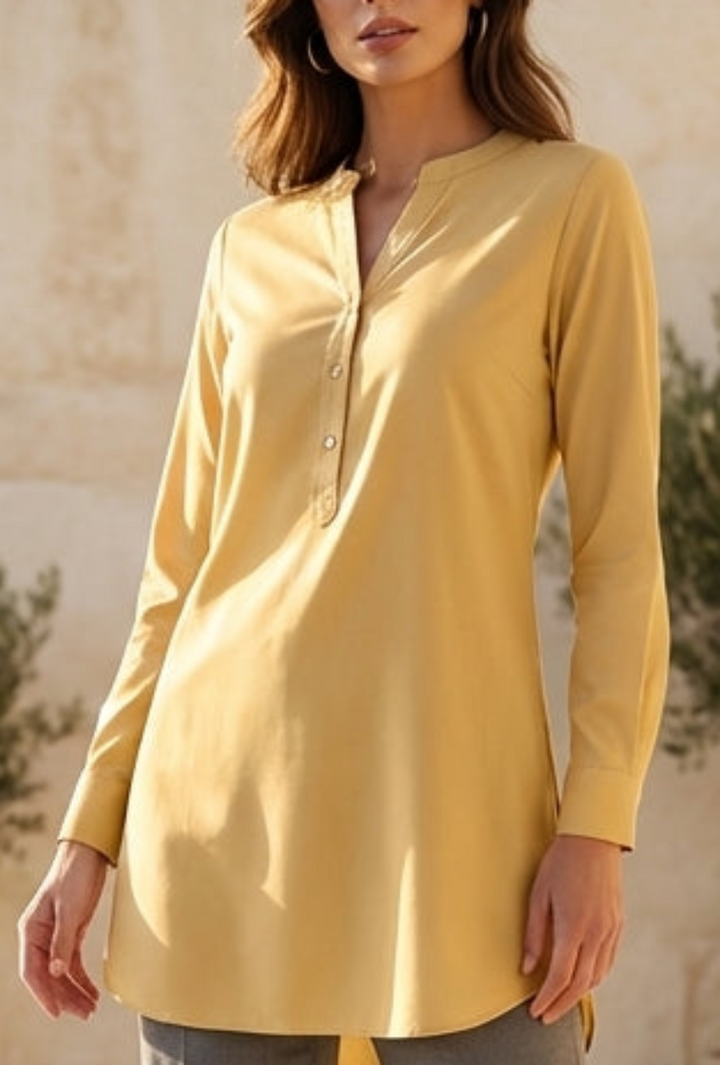 Woman in a yellow top and gray pants standing on a sunlit patio with plants and a scenic background.