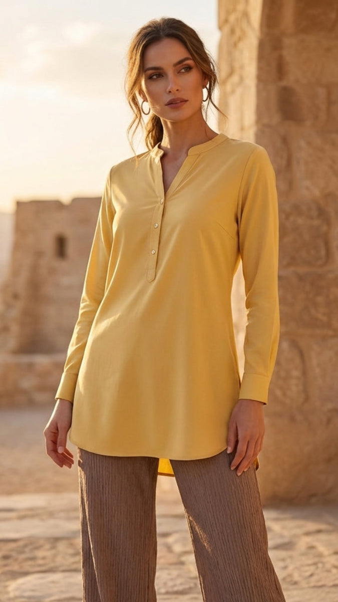 Woman wearing a yellow shirt and brown pants standing in front of a stone building.