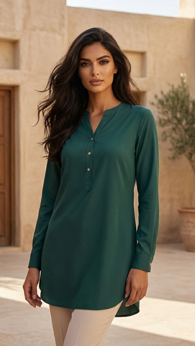 Woman wearing a green long-sleeve shirt standing in an outdoor setting with beige walls and a wooden door.