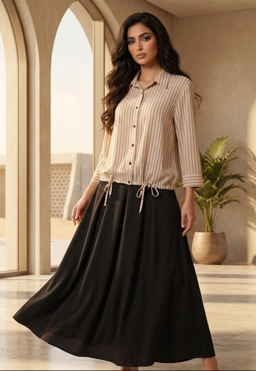 Woman in a beige top and black skirt standing in a modern interior setting with large windows.