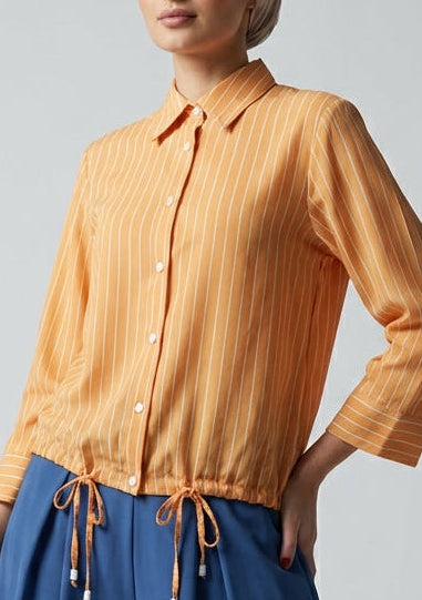 Woman wearing an orange blouse and blue pants against a gray background