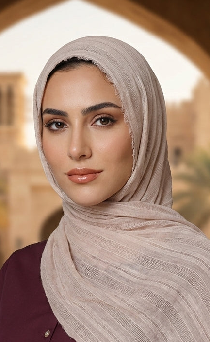 Woman wearing a beige hijab and maroon outfit in an outdoor setting with arches and greenery.