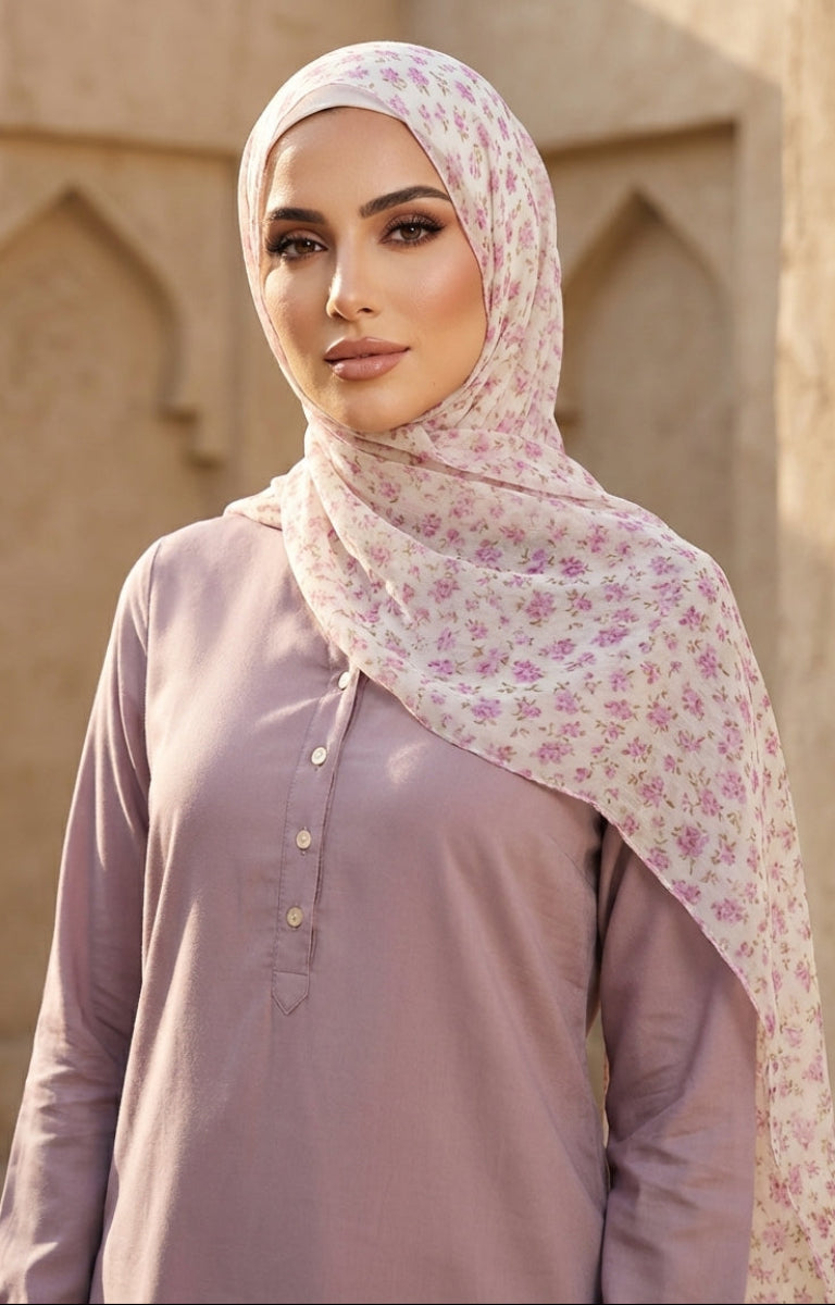 Woman wearing a floral hijab and light purple shirt in front of beige architectural background