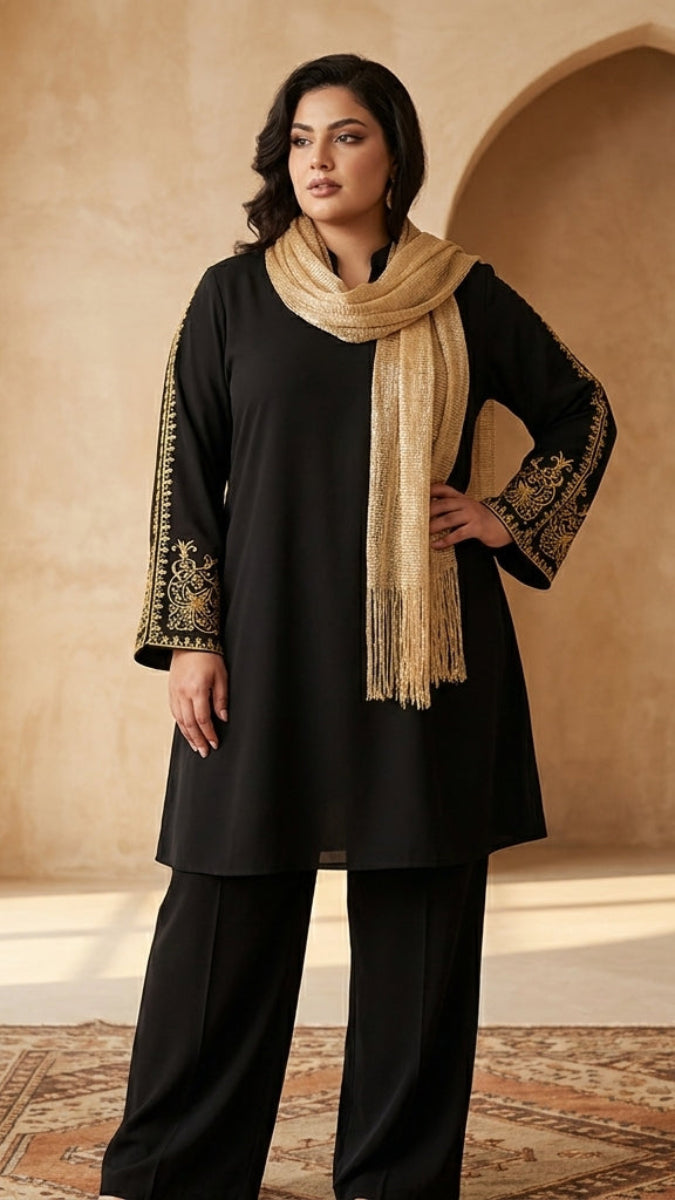 Woman wearing a black outfit with gold embroidery and a beige scarf in a sunlit room.