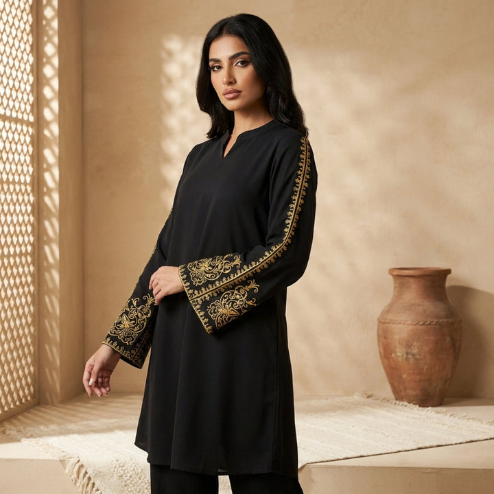 Woman wearing a black outfit with gold embroidery in a warm-toned room.