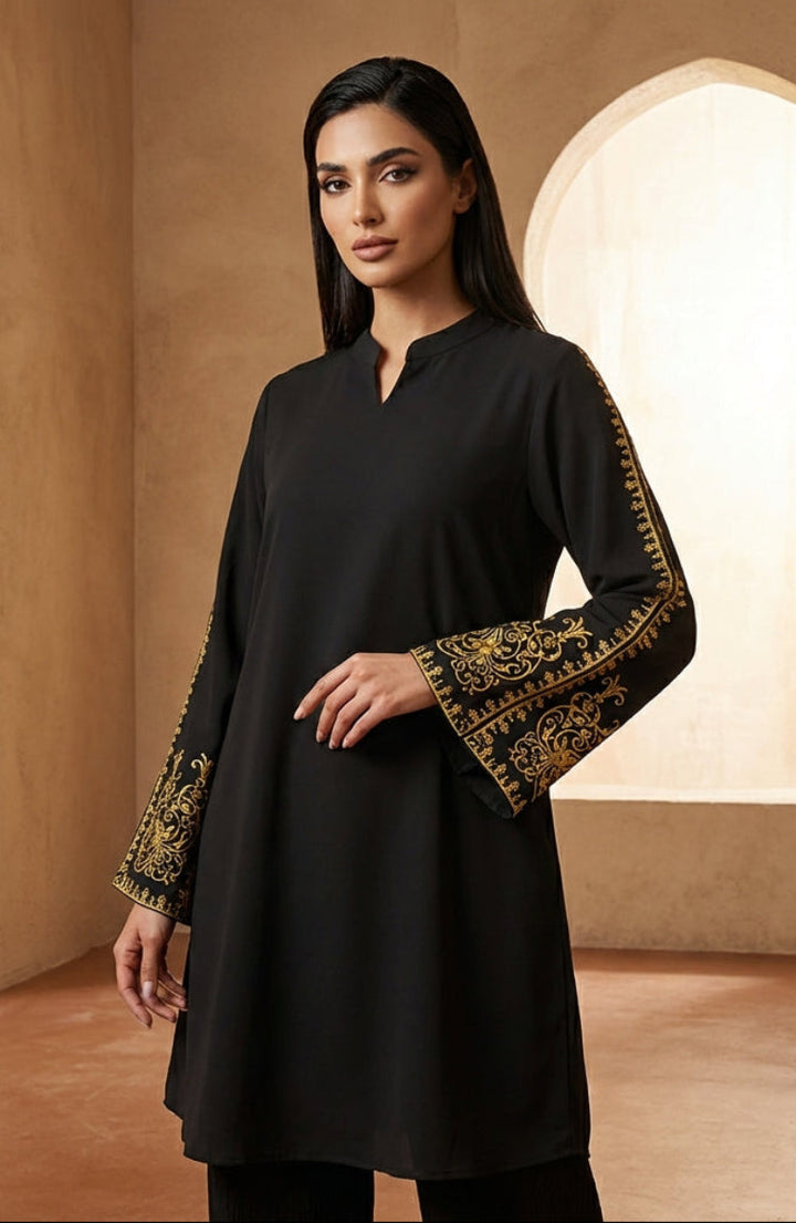 Woman wearing a black dress with gold embroidery in a warm-toned room.
