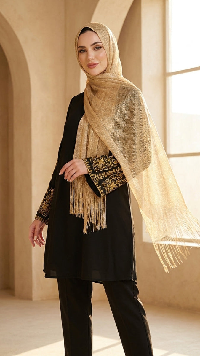 Woman wearing a beige hijab with gold patterns in a softly lit room.