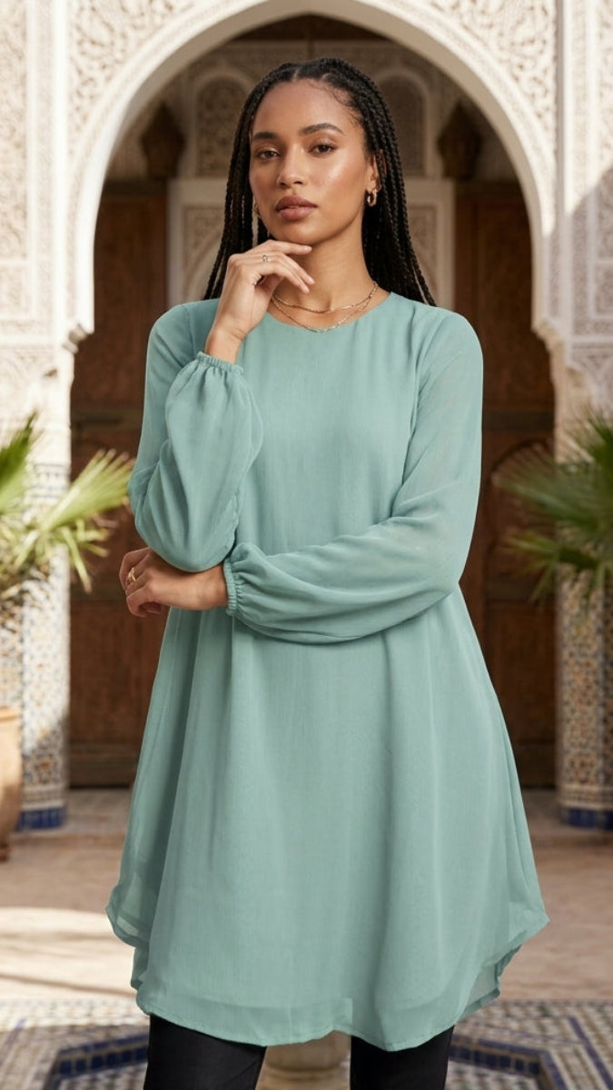 Woman in a light blue dress standing in a decorative courtyard with plants and arches.