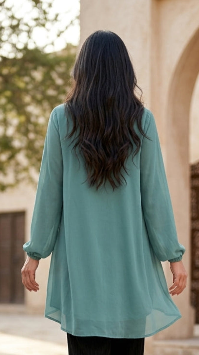 Woman in a teal dress walking away from the camera in an outdoor setting with architectural elements.