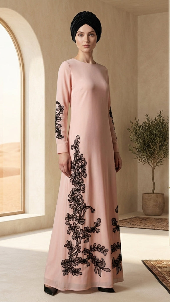 Woman in a pink dress with black embroidery standing in a room with a large window and plants.