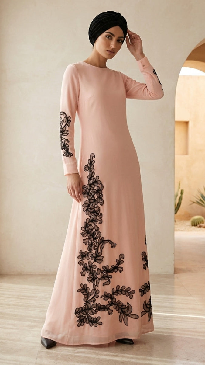 Woman wearing a pink dress with black embroidery in a bright room.