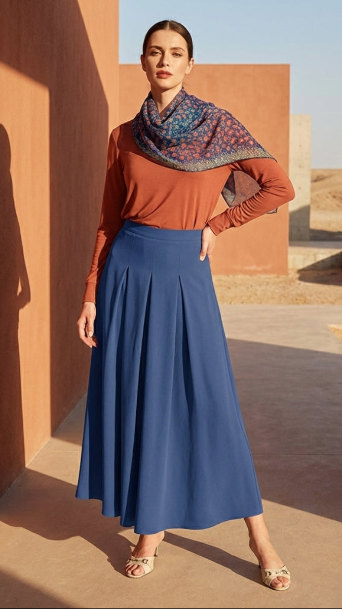 Woman in a blue skirt and orange top standing in a sunlit architectural setting.