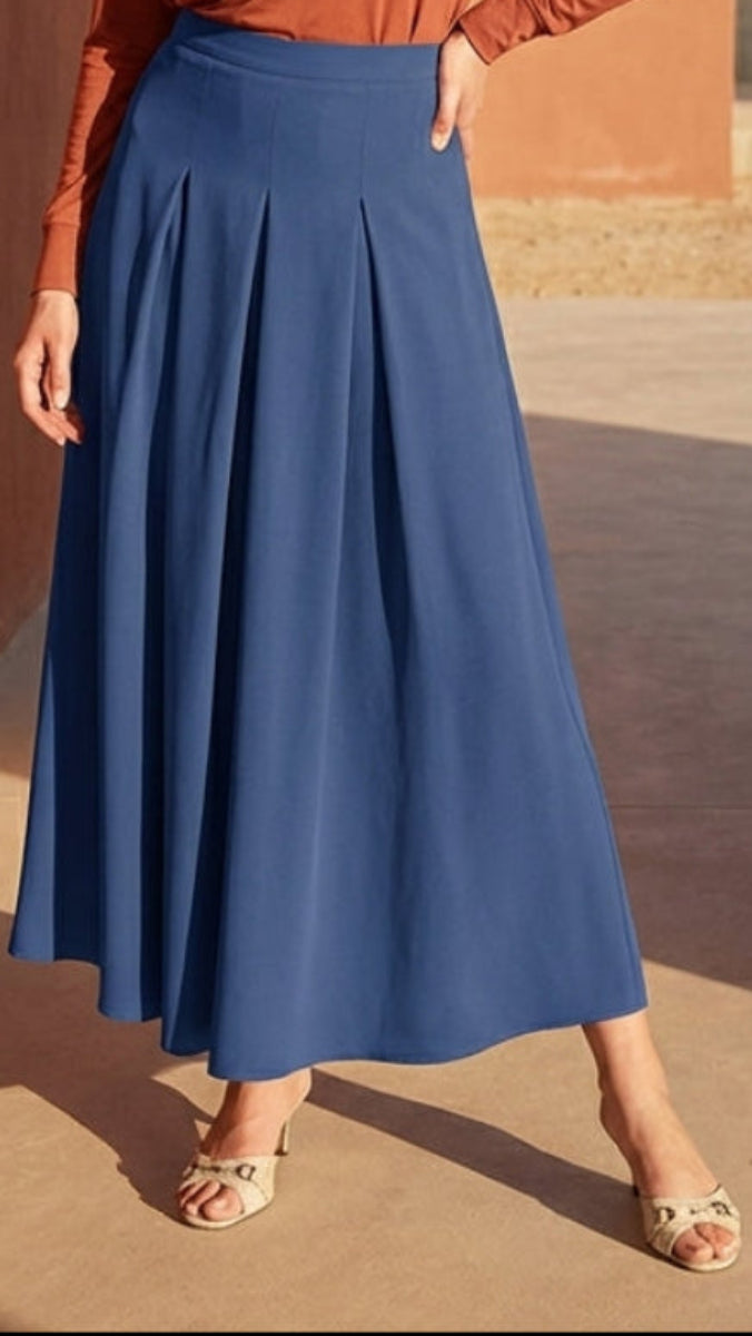 Woman wearing a rust-colored top and blue skirt with a patterned scarf outdoors.